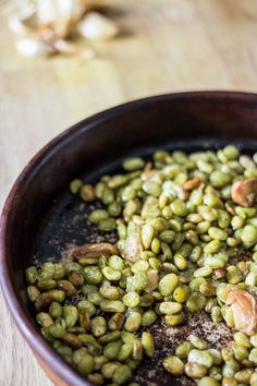 a bowl filled with green beans and nuts on top of a wooden table next to a spoon