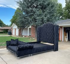 a black bed sitting in the middle of a driveway next to a tree and house