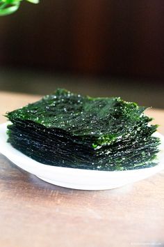 a white plate topped with green seaweed on top of a wooden table next to a potted plant