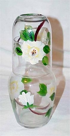 a glass vase with white flowers painted on it's sides and green leaves in the bottom