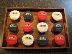 twelve cupcakes with different colored frosting faces on them in a wooden tray