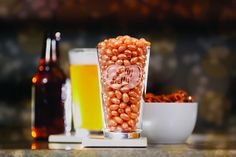 a glass filled with some kind of food next to a bottle and two cups full of beer