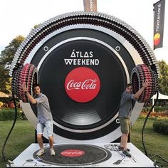 two people standing in front of a giant coca - cola sign with the words atlas weekend written on it