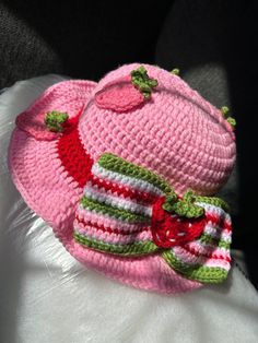 a pink crocheted hat with green and white stripes on the brim is sitting on a pillow