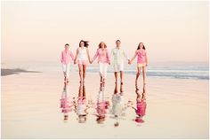 a group of people holding hands walking on the beach with water reflecting them in the wet sand