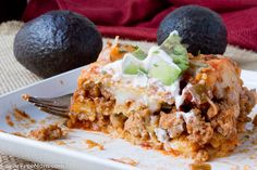 a piece of mexican casserole on a plate with two avocados in the background