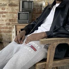 a man sitting in a chair wearing sweatpants and a leather jacket with his hands on his hips