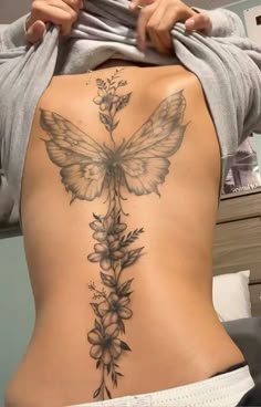 a woman's back with a butterfly tattoo on her lower body and flowers growing out of it