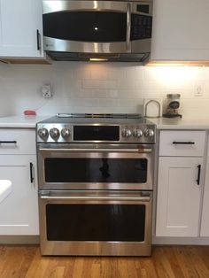 a stainless steel oven and microwave in a kitchen with white cabinets, wood flooring and wooden floors