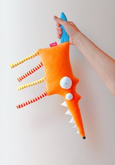 a hand holding an orange stuffed animal with spikes and teeth on it's back