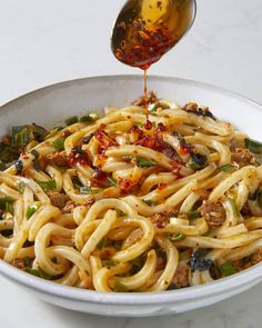 a spoon is pouring sauce over a bowl of noodles