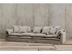 a couch with many pillows on it sitting in front of a concrete wall and wooden floor