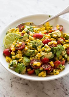 a white bowl filled with corn, avocado, tomatoes and cilantro