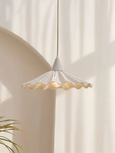 a white lamp hanging from a ceiling next to a potted plant