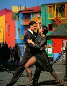 a man and woman dancing in front of colorful buildings