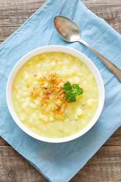 a white bowl filled with soup on top of a blue napkin next to a spoon