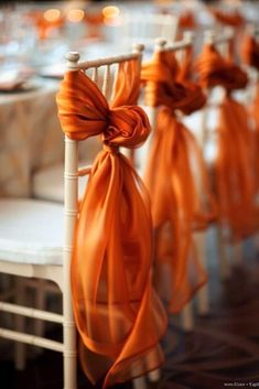 an orange ribbon tied to the back of a white chair at a wedding banquet table