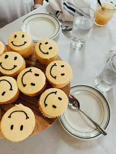 cupcakes with faces drawn on them sitting on a wooden platter at a table