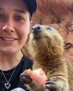 a woman holding up a piece of salmon in front of an animal that is standing on its hind legs