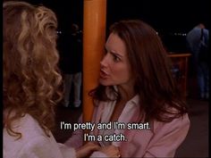 two women talking to each other in front of an orange pole with the words i'm pretty and i'm smart, i'm a catch