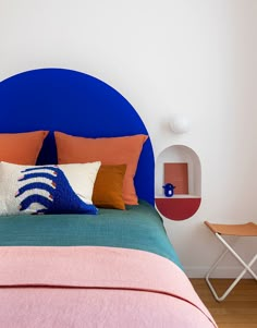 a bed with blue headboard and colorful pillows on it's sides, against a white wall