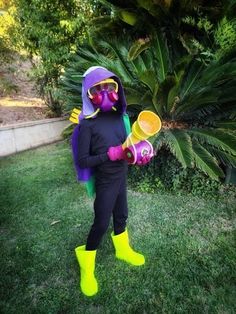 a person in a purple and green costume holding two yellow plastic cups while standing on some grass