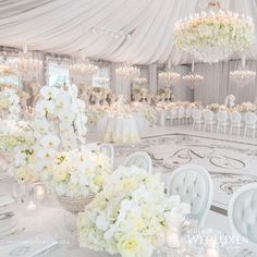 the tables are set up with white flowers and centerpieces for an elegant wedding reception