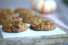 chocolate chip cookies sitting on top of a white plate next to an orange and green pumpkin