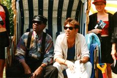 a man sitting in a chair next to other people wearing hats and sunglasses on the beach