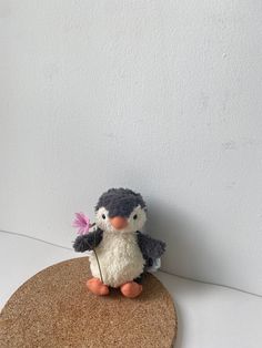 a small penguin holding a flower on top of a cork coaster with a white wall in the background