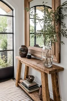 a wooden bench sitting under a window next to a vase with a plant in it