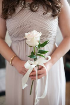 a woman in a dress holding a white rose and wearing a wedding band on her wrist