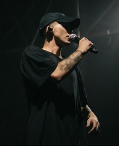 a man with tattoos on his arm holding a microphone in front of a dark background