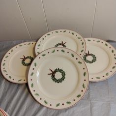 four christmas plates with holly wreaths on them sitting on a tablecloth covered surface