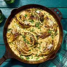 an iron skillet filled with artichokes covered in cheese and parsley