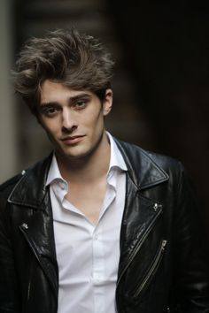 a young man wearing a black leather jacket and white shirt is looking at the camera