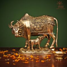 a brass cow and calf statue on a wooden table with orange petals scattered around it