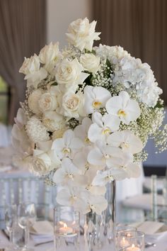 white flowers and candles are arranged in tall vases