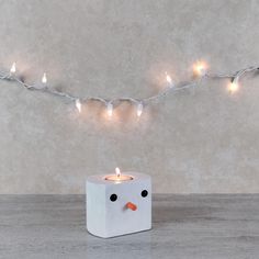 a small white candle holder with a lit up penguin face on it's side