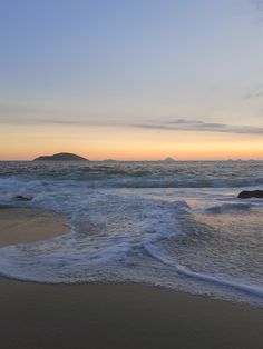 the waves are coming in to the shore at sunset on an empty beach with small islands in the distance