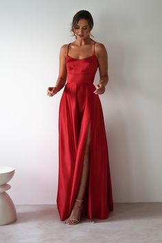 a woman in a long red dress standing next to a white wall and smiling at the camera