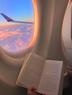 a person is reading a book while flying in the sky with an airplane window behind them