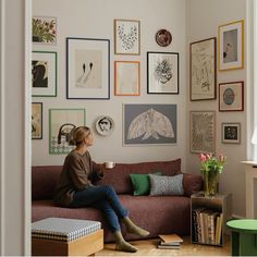 a woman sitting on top of a couch in front of a wall filled with pictures