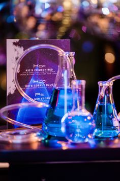 blue flasks and beakles sit on a table in front of a business card