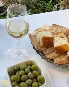 bread and olives are on a table next to a glass of white wine,