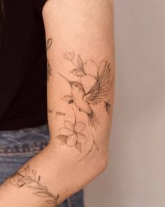 a woman's arm with flowers and a bird tattoo on the left side of her arm