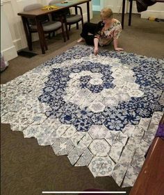 a woman sitting on the floor next to a large blue and white rug in a room