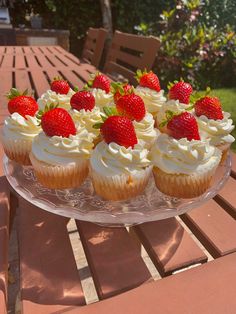 cupcakes and strawberries on a glass platter sitting on a table outdoors