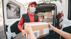 two people unloading boxes from the back of a white van, one wearing a face mask