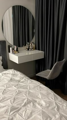 a white bed sitting next to a mirror on top of a dresser under a window